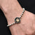 Boys' bracelet featuring white beads and a silver flower logo.